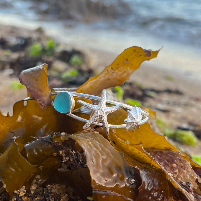 Sterling silver split centre cuff featuring a cast silver limpet shell and sea star as well a blue sea glass gem. 60cm diameter with a 3cm opening.By Mornington Sea Glass.